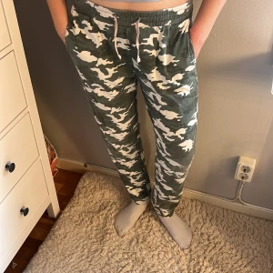 Camo mjukisbyxor från XOXO Friends - Gröna och vita mjukisbyxor från XOXO Friends med camouflagemönster. Byxorna har resår i midjan med snörning och raka ben. 