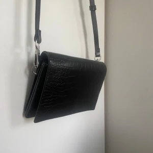 Svart axelväska i skinn - Snygg svart axelväska från Carin Wester i skinn med bred axelrem och smal axelrem. Väskan har magnetlås, innerfack med dragkedja och stilren design. 