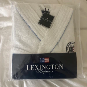 Vit Lexington frottébadrock -  Vit badrock från Lexington i mjuk frotté med broderad logga på bröstet och diskreta blå detaljer längs kanterna. Oöppnad och oanvänd. Orginalpris 1995 kr. 