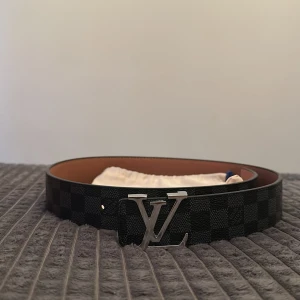 Svart bälte  - Snyggt bälte i svart med klassiskt rutigt Damier-mönster och silverfärgat logg-spänne. Bältet är gjort i exklusivt skinn och har en stilren design som lyfter vilken outfit som helst. Kommer med originalpåse och box.