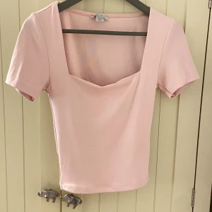 Ljusrosa topp med fyrkantig ringning Amisu - Supersöt ljusrosa topp från Amisu med korta ärmar och snygg fyrkantig ringning. Modellen är croppad och har en enkel, stilren design som passar perfekt till jeans eller kjol. Mjuk och stretchig bomullsblandning för skön passform.