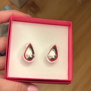 Silverfärgade droppformade örhängen SNÖ - Snygga droppformade örhängen från SNÖ of Sweden i blank silverfärg. De har en stilren och modern design som verkligen poppar. Perfekta för dig som gillar minimalistiska smycken med en twist.