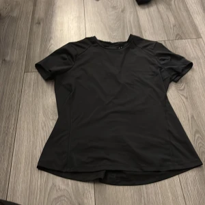 Svart träningstopp från SOC - Svart teknisk träningstopp från SOC i storlek M. T-shirten har rund hals, korta ärmar och är tillverkad i ett lätt och snabbtorkande syntetmaterial som andas. Perfekt för gymmet eller löprundan. Diskret logga framtill och bak.