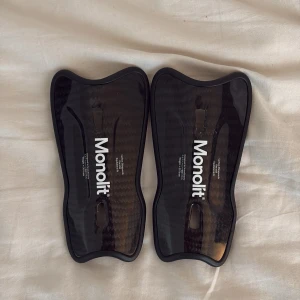 Monolit Carbon Fiber Shin Guards - Lätta, de små och slitstarka benskydd i kolfiber från Monolit. Ergonomisk design för optimal komfort och skydd. Båda skydden är i mycket gott skick utan synliga repor eller skador. Perfekt för fotbollsspelare som söker högsta prestanda och stil. 
