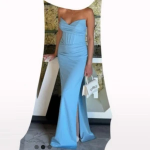 Ljusblå långklänning med snörning - Supersnygg ljusblå långklänning med axelbandslös design och v-ringad överdel. Klänningen har figurnära passform, slits framtill och snygg snörning i ryggen. Materialet är mjukt och följsamt, perfekt för att sticka ut på bal eller student. Stilren och modern look.