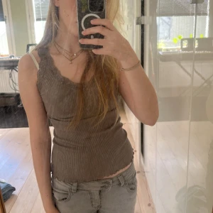 Ribbad grå linnetopp med spets - Supersöt ribbad grå linnetopp från Bompys & Sindong med v-ringning och spetsdetaljer längs kanterna. Toppen är väldig streckig och har vågig kant nertill. mjukt material som känns skönt mot huden. Skulle säga att toppen passar S-M