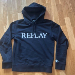Svart hoodie från Replay - Svart hoodie från Replay i storlek XS med stor vit logga framtill. Klassisk huva med snörning och långa ärmar. Mjuk och skön bomullsblandning, perfekt för chill dagar eller när du vill ha en clean streetstyle-look.