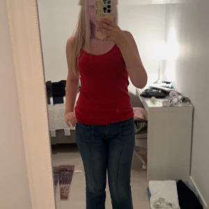 Röd linnetopp med smala axelband - Enkel och snygg röd linnetopp från Cubus med smala axelband och v-ringning. Toppen är ärmlös och har en figurnära passform, perfekt till jeans eller kjol. Mjuk och skön bomullskvalitet som känns lätt på kroppen.