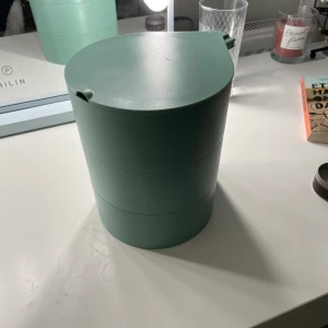 Grön smink- och smyckesförvaring med spegel - Praktisk grön förvaringsbox i plast med tre våningar och inbyggd spegel. Varje våning har olika fack för smycken, smink eller småprylar. Snygg och modern design, i mycket fint skick utan synligt slitage. Perfekt för organiserad förvaring på sminkbordet.