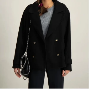 Svart kappa - Kappa med dubbelknäppning och bred krage. Jackan har en loose passform, stora fickor framtill och är tillverkad i en mjuk ullmix. Accepterar bud!