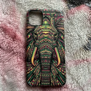 iPhone 11 Pro Max Skal med Elefantmönster - Färgglatt skal till iPhone 11 Pro Max med unikt elefantmönster i tribal-stil. Skalet är i gott skick men har mindre slitage i hörnet. Ger bra skydd och personlig stil till din mobil. Vid frågor hör av dig!