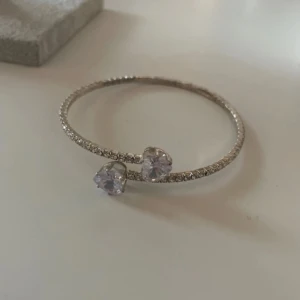 Silverfärgat armband med hjärtformade stenar - Ett elegant armband i silverfärg med gnistrande små stenar längs hela bandet och två större hjärtformade stenar i ändarna. Perfekt för dig som gillar stilrena och romantiska smycken med lite extra bling.
