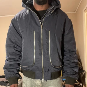 Vinter puffer bomberjacka HOPE - En stilren puffer bomberjacka från HOPE i marinblå helt ny skick. Jackan är fodrad och varm samt har en luva. Den har dubbla dragkedjor framtill i junisex, och passar storlek M/L för her och L/XL för dam. Säljer den så jag brukar bära S vanligtvis men va så sugen på denna jacka. 