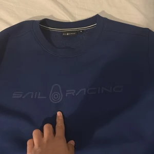 Blå Sail Racing sweatshirt i bomull - Mörkblå sweatshirt från Sail Racing med diskret logga framtill. Klassisk rund halsringning och långa ärmar. Tillverkad i mjuk bomull, perfekt för chill dagar eller när du vill ha en clean look.