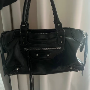 Handväska  - Svart väska med silvriga detaljer. Liknar en Citybag. Några små trådar som sticker ut vid handtagen. I övrigt i väldigt bra skick. 38 x 24cm 