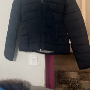 Svart pufferjacka från Hollister M - Svart pufferjacka från Hollister i storlek M. Jackan har huva, dragkedja framtill och är fodrad med mjuk vit teddy på insidan. Perfekt för kyliga dagar och har en clean, stilren look som funkar till det mesta.