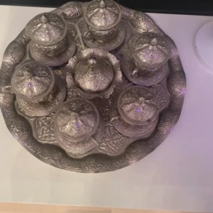 Minor Cafe House - Bilderna visar ett vackert dekorerat set med orientaliska kaffekoppar och fat i metall, komplett med lock och serveringsbricka. Setet har fina mönster och ser ut att vara i gott skick utan synliga skador. Perfekt för servering av kaffe eller som dekorativt inslag i hemmet.