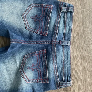 Blå bootcut jeans med röda sömmar - Snygga blå jeans från Gina Tricot 14+ med bootcut-modell och markerade röda sömmar. Jeansen har fina fickor med coola detaljer på bakfickorna. Stl S och säljes pga att dom är för korta för mig, använda ca 1 gång. Tvättar innan jag skickar💕Pris kan diskuteras
