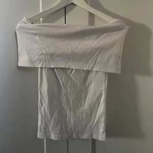 Vit offshoulder tubtopp - Säljer en stilren vit offshoulder topp. Toppen är enkel och rak i modellen, perfekt att matcha med jeans eller kjol. Mjuk och skön känsla, men formar sig efter kroppen!
