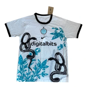 Inter Milan x Nike vit fotbollströja - Inter Milan fotbollströja i vitt med svarta och turkosa detaljer, svart krage och ärmslut. Unikt grafiskt mönster med ormar och blå växtmotiv framtill. Tillverkad i lätt och ventilerande polyester, perfekt för match eller träning.
