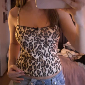 Leopardmönstrad linnetopp med rosett - Säljer en snygg leopardmönstrad linnetopp med smala axelband och liten svart rosett framtill. Toppen är figurnära och har svarta detaljer längs kanten. Perfekt för dig som vill sticka ut med ett djurmönster.