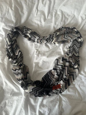 Grå/svart halsduk från Missoni - Snygg halsduk från Missoni med ikoniskt zigzag-mönster i svart, grått, beige och vitt. Halsduken är stickad och har en mjuk känsla, perfekt att slänga över axlarna för en cool och trendig look. Passar dig som gillar statement-accessoarer. Längd: ca 190cm Bredd: ca 40cm