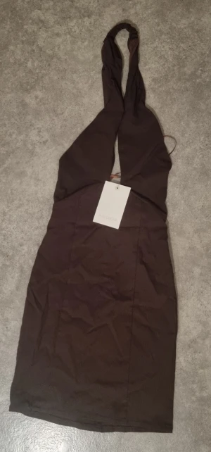 Brun halterneck klänning Pull&Bear - Snygg brun kort klänning från Pull&Bear med halterneck och åtsittande passform. Klänningen har en stilren design utan mönster och är perfekt för dig som gillar trendiga och enkla plagg. Materialet känns mjukt och följsamt.