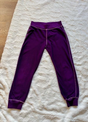 Lila underställsbyxor från Outwear - Mysiga lila underställsbyxor från Outwear med bred resår i midjan och kontrastsömmar. Perfekta för kalla dagar eller som lager under andra byxor. Mjukt material som känns skönt mot huden.