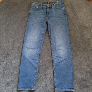 Blå jeans från Jack & Jones - Snygga blå jeans från Jack & Jones. Jeansen har regular fit, raka ben och normal midja. Tillverkade i mjukt denimtyg med lätt tvättad look och diskreta slitningar. Perfekta för en avslappnad stil. 