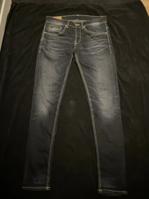 Dondup Mörkblå/grå  - Snygga mörkblå jeans med skinny passform och kontrastsömmar. Klassisk femficksdesign, ljusa slitningar framtill och bak, samt detaljerade bakfickor. Perfekt för dig som gillar en smal siluett och stilrena detaljer.