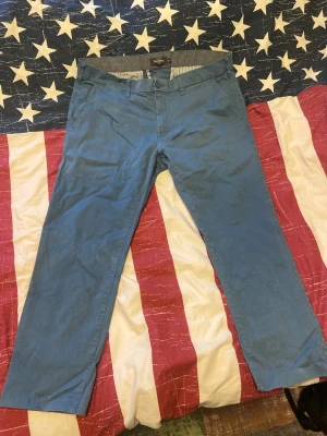 Blå chinos från Dressmann slim fit - Snygga blå chinos från Dressmann i slim fit-modell. Byxorna har klassisk rak passform, bälteshällor, knappstängning och fickor både fram och bak. Materialet är mjukt och skönt bomullstyg, perfekt för en clean och stilren look. Byxorna har jag klippt och sytt själv eftersom de var lite för långa för mig. Storlek 38/32. Byxorna har hållits i gott skick. 