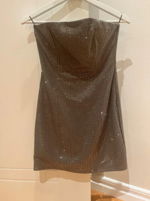 Glittrig silver kort klänning från Zara - Säljer en superfin axelbandslös kort klänning från Zara i silver med glittriga paljettdetaljer. Klänningen har en tight passform och är perfekt för dig som vill sticka ut. Materialet är mjukt och följsamt, vilket gör den bekväm att bära hela kvällen.