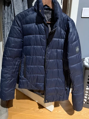 Mörkblå Replay jacka - Snygg mörkblå pufferjacka från replay. Jackan har dragkedja framtill, två sidofickor och en diskret logga på ärmen. Perfekt för kalla dagar och har en clean, modern look.