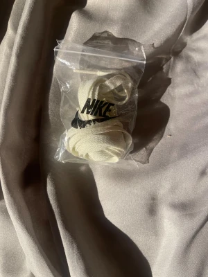 Vita Nike skosnören i originalpåse - Fräscha vita skosnören från Nike, levereras i original plastpåse med svart Nike-logga. Perfekt för att ge dina sneakers en clean och fräsch look. Skosnörena är platta och tillverkade i slitstark syntet för bästa hållbarhet.