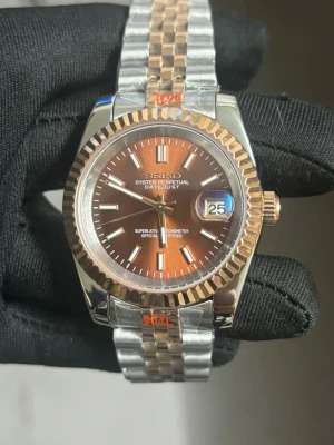 Seiko Datejust brun/silver/guld klocka - Snygg Seiko Oyster Perpetual Datejust med brun urtavla och datumvisning. Klockan har en tvåfärgad länk i silver och guld samt räfflad bezel i guldton. Automatisk rörelse synlig på baksidan. Perfekt accessoar för dig som gillar klassisk stil med modern touch. Snabb affär = lägre pris 