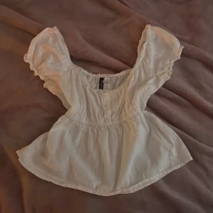 Söt babydoll topp - Supersöt vit blus med puffiga korta ärmar och elastisk kant som kan bäras offshoulder. Blusen har knappar framtill, markerad midja och lätt volang nedtill. (Den har gula fläckar som inte syns men går att tvätta bort!)