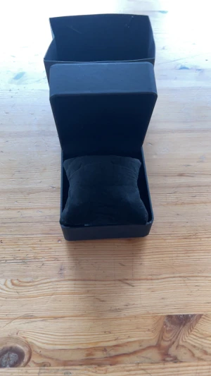 Svart klockask med kudde - Säljer en stilren svart klockask med matchande kudde inuti. Asken har en enkel och modern design med mjuka linjer och är perfekt för att förvara din klocka. Kudden är klädd i svart tyg och ger extra skydd. Perfekt för dig som vill ge bort en klocka eller förvara din egen.