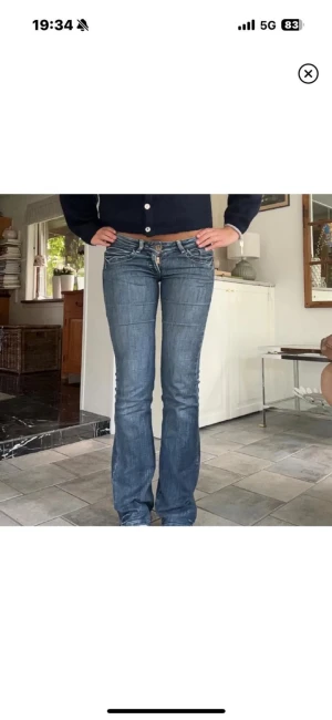 Blå bootcut jeans med låg midja - Snygga blå jeans med bootcut och låg midja. Jeansen har klassiska fickor fram och bak med dekorativa sömmar på bakfickorna. Perfekt passform som sitter tajt upptill och släpper vid benen. Tillverkade i jeansmaterial.