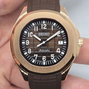 Seikmod automatisk klocka i guld och brunt - Snygg automatisk klocka Seikmod med fyrkantig boett i guldfärgad metall och brunt rutmönstrat urtavla. Brunt gummiband med struktur och datumvisning vid klockan tre. Perfekt accessoar för dig som gillar stilren design med lyxig känsla.