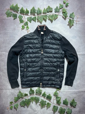 Moncler Tricot Cardigan i Navy Storlek S [ÄKTA] - 🎨 Färg: Mörkblå / Navy 📏 Storlek: S ♻️ Skick: 8/10 – En synlig fläck på backsidan. Inga hål eller skador 🧵 Material: Quiltad lättvikt framtill + mjuka stickade/fleece-liknande ärmar och rygg ✨ Detaljer: • Hybridmodell med dun/quiltad front och tygärmar • Hög krage • Två framfickor med knappar och dragkedjedetaljer • Moncler-patch på vänster ärm • Tvåvägsdragkedja framtill • Klassisk, stilren och bekväm design ‼️ Skickas dagen efter köpet genomförs! ‼️ 