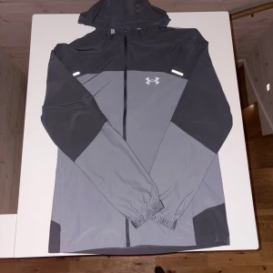 Under Armour jacka  - Under Armour jacka i toppskick 🩶 Snygg och funktionell jacka i grå/svart som funkar perfekt till både träning och vardag. Lätt, bekväm och med riktigt bra passform. Vindavvisande material + reflexdetaljer gör den praktisk året runt.  Skick: Väldigt fint – knappt använd ✨ Storlek: M  En stilren och pålitlig jacka för dig som vill ha något som bara funkar 👍