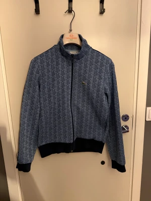  Zip hoodie Lacoste  - Snygg blå zip hopdie från Lacoste med geometriskt mönster och klassisk krokodillogga på bröstet.Passar både xs/S.         Nästan helt ny använd ett fåtal gånger skriv vid frågor och pris kan diskuteras