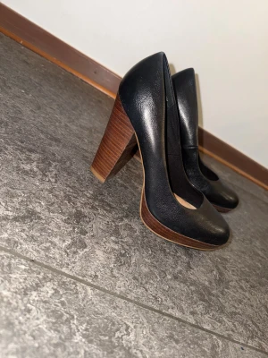 Svarta pumps med träklack från XIT - Snygga svarta pumps från XIT i storlek 39. Skorna har rund tå, hög träklack och plattform framtill. Tillverkade i skinnimitation med en stilren och klassisk look som passar till många outfits.