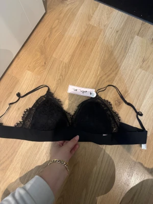 Svart spets bandeau från Ella M. - Säljer en svart spets bralette  från Ella M. med snygga spetsdetaljer och justerbara axelband. Toppen har en bred elastisk kant under bysten och är axelbandslös med en feminin look.  Helt oanvänd med prislappen kvar nypris 299kr. 