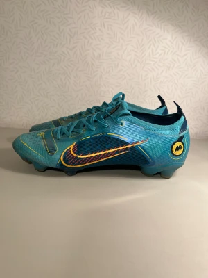 Nike Mercurial Vapor  fotbollsskor - Säljer ett par Nike Mercurial Vapor fotbollsskor i en snygg blå färg med gula och röda detaljer. Skorna har snörning, låg profil och är tillverkade i syntetmaterial med Flyknit-teknologi för extra komfort och passform. Perfekta för dig som vill sticka ut på planen, inga tecken på trasiga. Skicka gärna frågor 