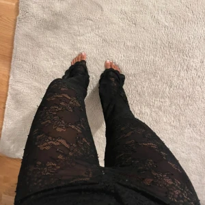 Svarta spetsbyxor med utsvängda ben från Zara - Säljer ett par svarta byxor i genombruten spets med utsvängda ben. Byxorna har en tight passform upptill och är transparenta med snyggt blommönster i spetsen. Perfekta för dig som vill sticka ut med en trendig look.