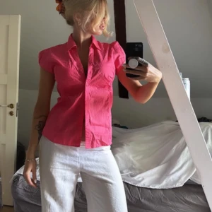 Rosa kortärmad blus med krage - Säljer en rosa blus i bomull med korta ärmar och klassisk krage. Modellen är figurnära med knappar framtill och lätt v-ringad öppning. Perfekt för dig som gillar färg och enkel stil. Storlek M.
