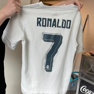 Äkta Real Madrid Ronaldo 7 matchtröja Adidas - Vit Real Madrid fotbollströja med Ronaldo 7 tryck på ryggen,Köpt i Santiago Bernabeu arena.Säljer i med att den är förliten pris kan diskuteras säljer lite billigare för de lilla hålet vid bröstkorgen .