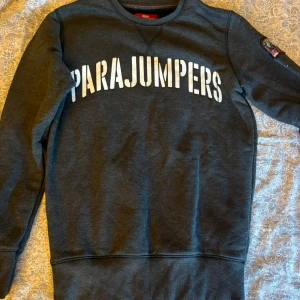 Mörkgrå sweatshirt från Parajumpers - Snygg mörkgrå sweatshirt från Parajumpers med stort vitt tryck över bröstet. Klassisk rund halsringning och långärmad modell. Perfekt för dig som gillar stilrena och sportiga plagg med tydlig logga.