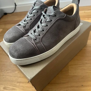 Grå Christian Louboutin - Snygga grå sneakers i mocka från Christian Louboutin med klassisk vit sula och ikonisk röd undersida. Skorna har rund tå, grå snörning och beige innersida. Perfekta för dig som vill ha en stilren och lyxig look med en touch av Paris. !PRIS KAN SÄNKAS VID SNABB AFFÄR!